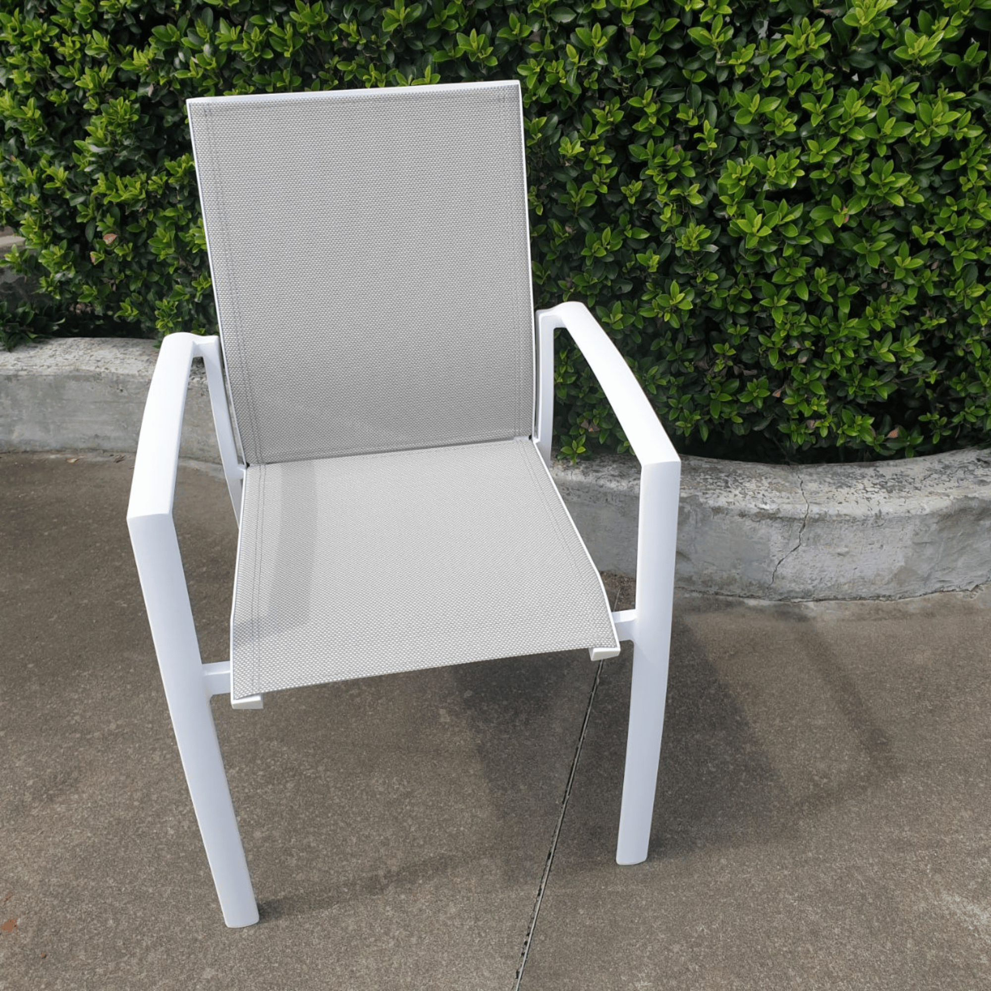 A white aluminium Florida outdoor dining chair with beige textilene sling seat and backrest, displayed on a concrete surface with greenery in the background.