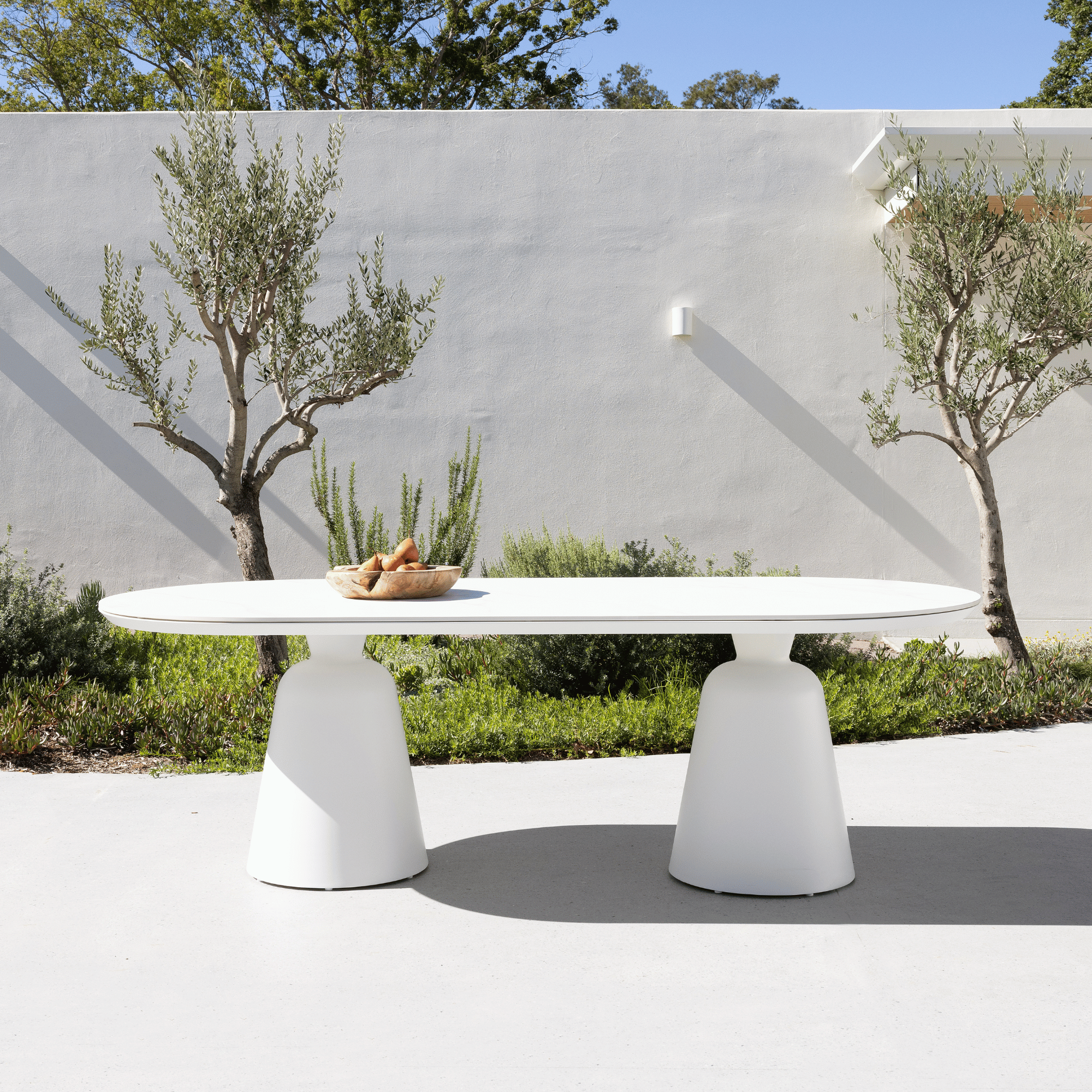 Modern outdoor table with a white base and round top in a garden setting.
