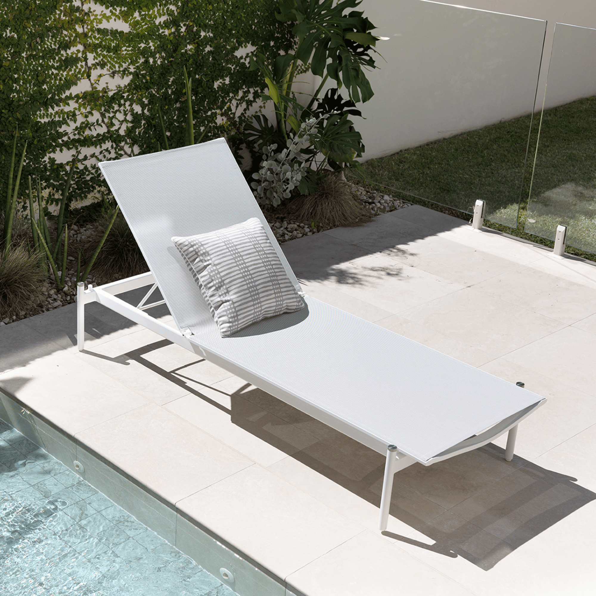 White lounge chair with a pillow by a poolside