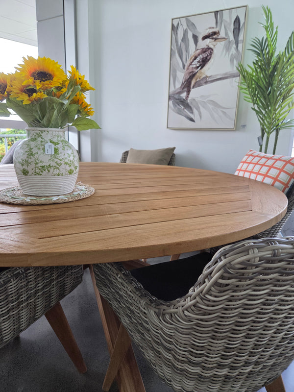 Round wooden table with a vase of sunflowers and wicker chairs, with a large canvas Kookaburra print on the wall