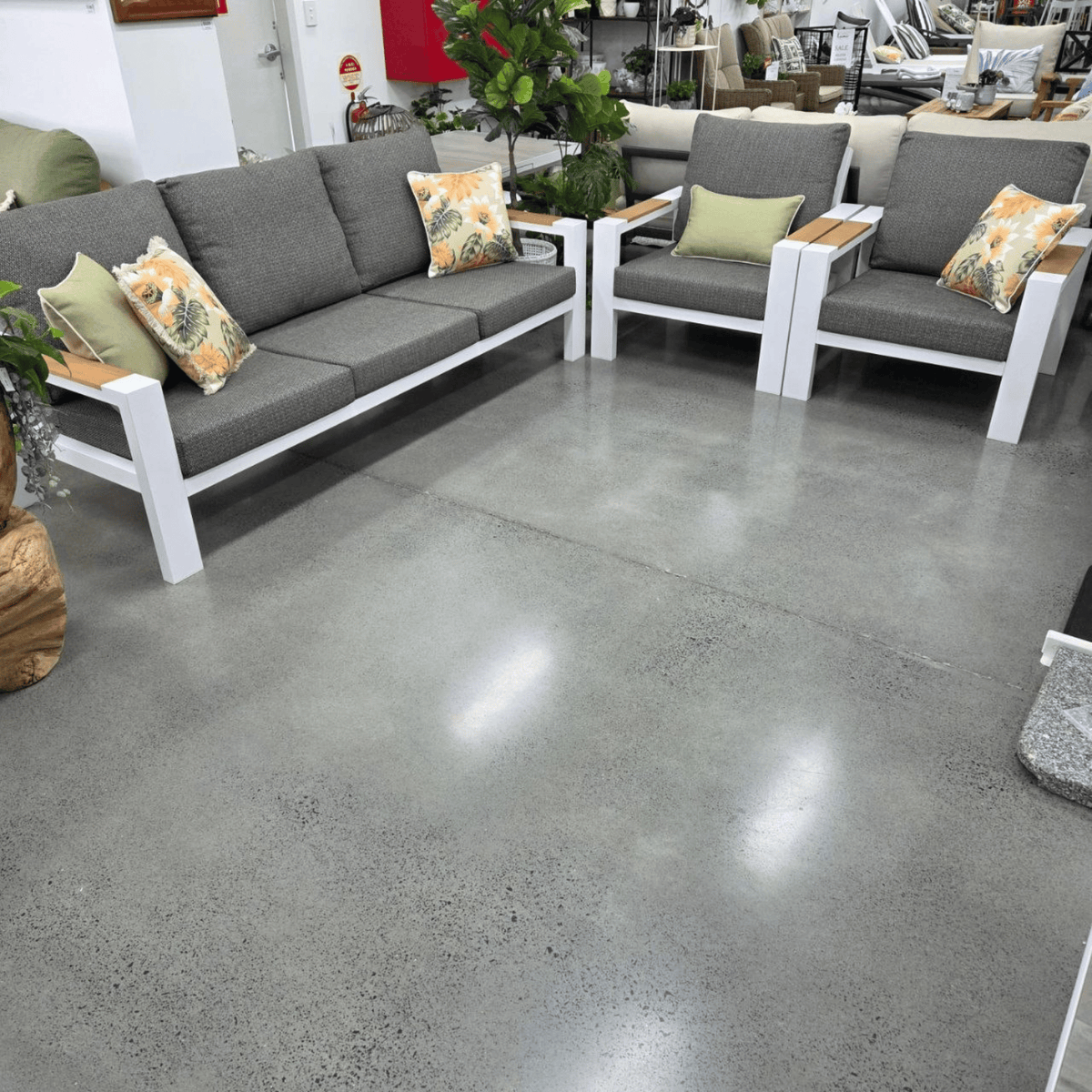 A modern Aspen outdoor patio furniture set featuring a grey fabric sofa and two matching armchairs with white frames and light wood armrests, styled with accent pillows on a polished concrete floor.