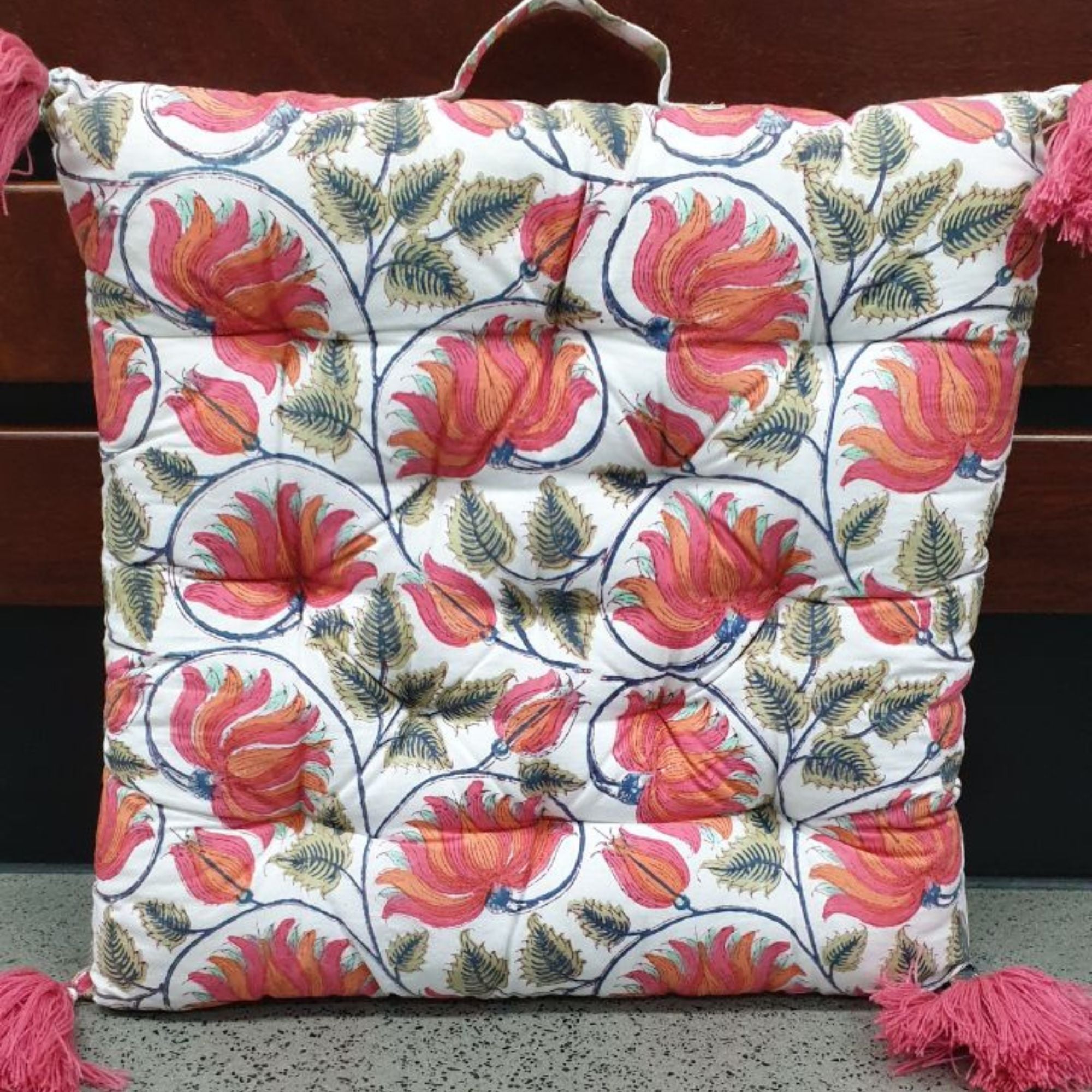 Decorative pillow with floral pattern and tassels on a wooden surface. DWBH Chair Pad - Reversible - Musk Medallion