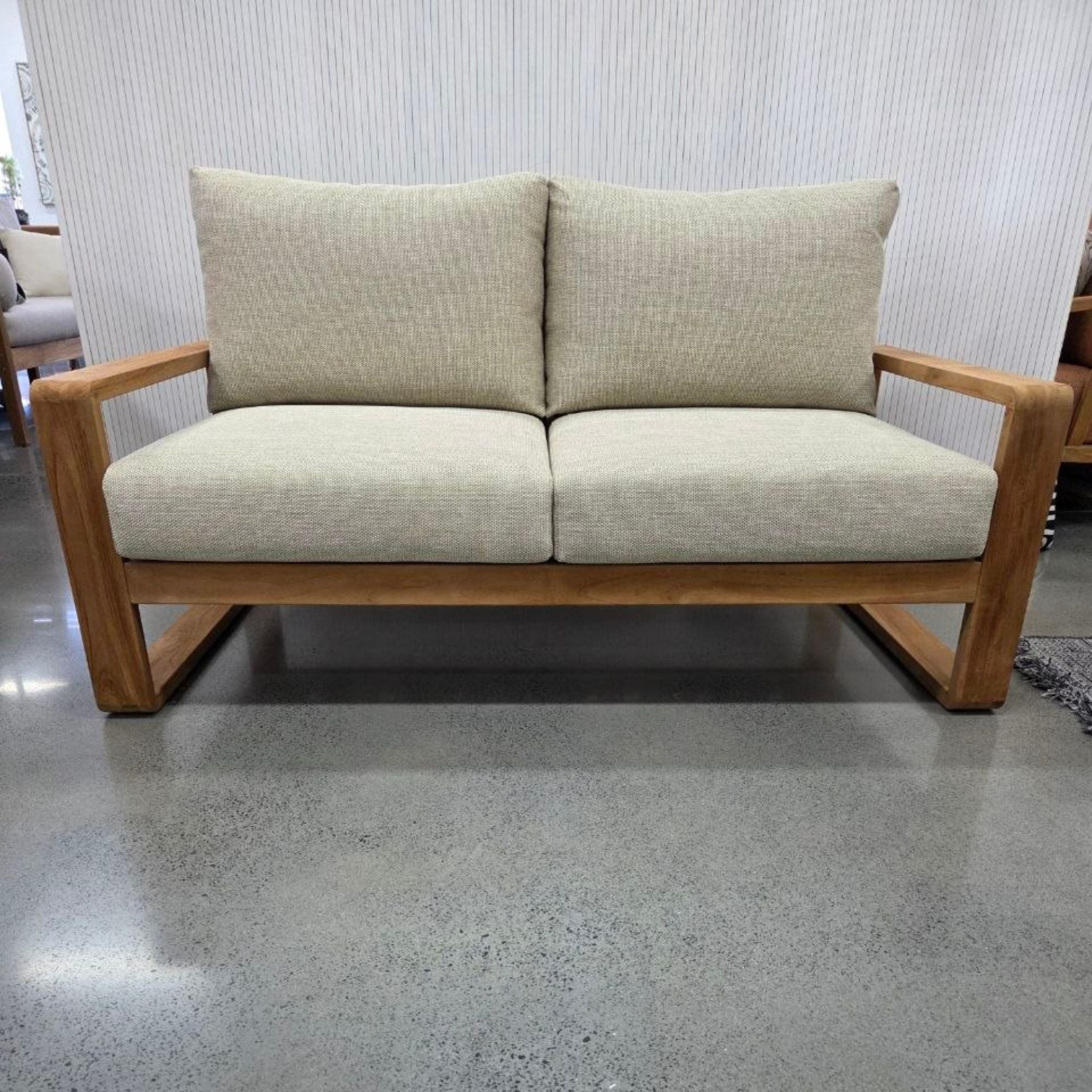 Two-seater sofa with wooden frame and light gray cushions on a gray floor.