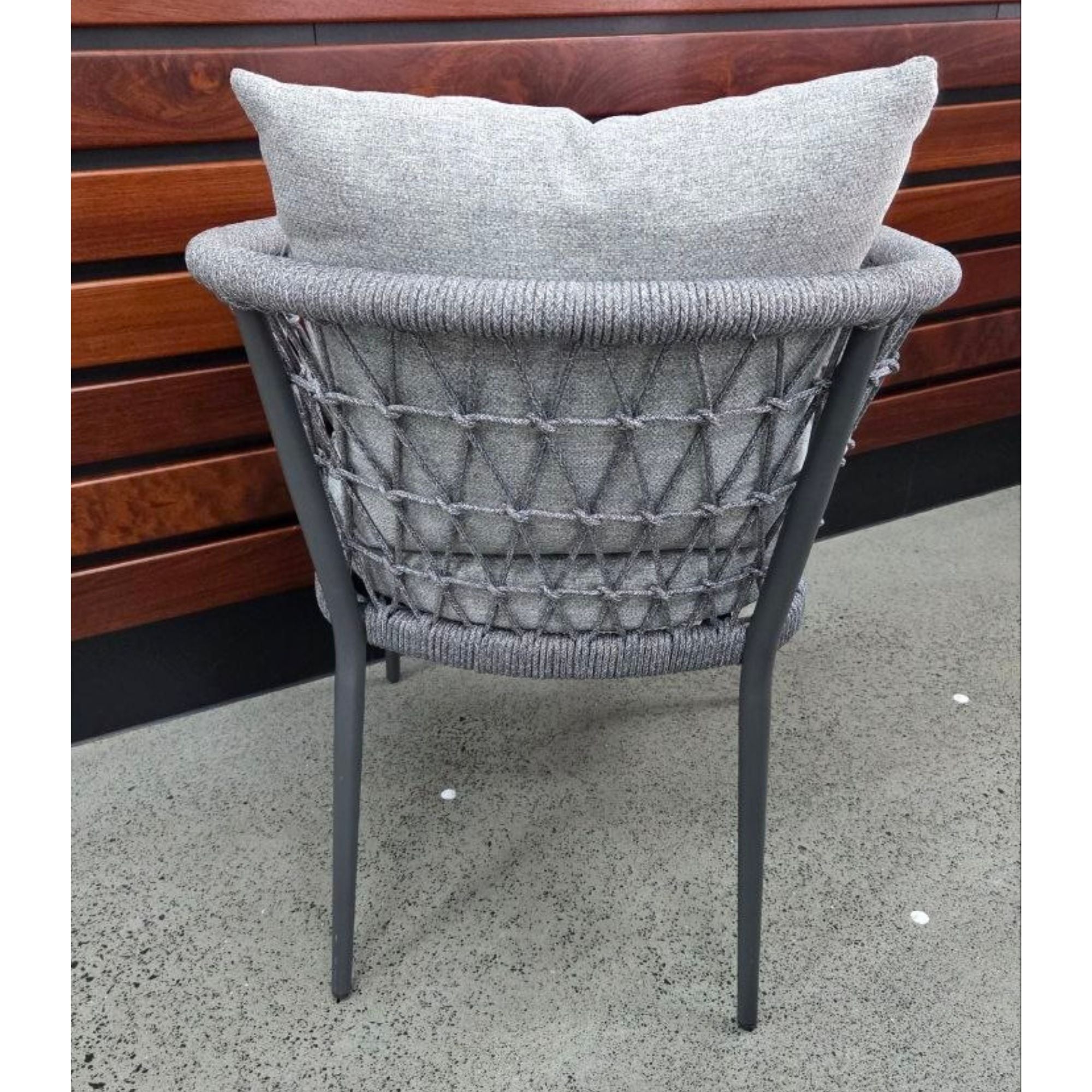 Back view Kinsley Dining Chair - Charcoal frame and grey rope weave with back and seat cushions, against a wooden wall