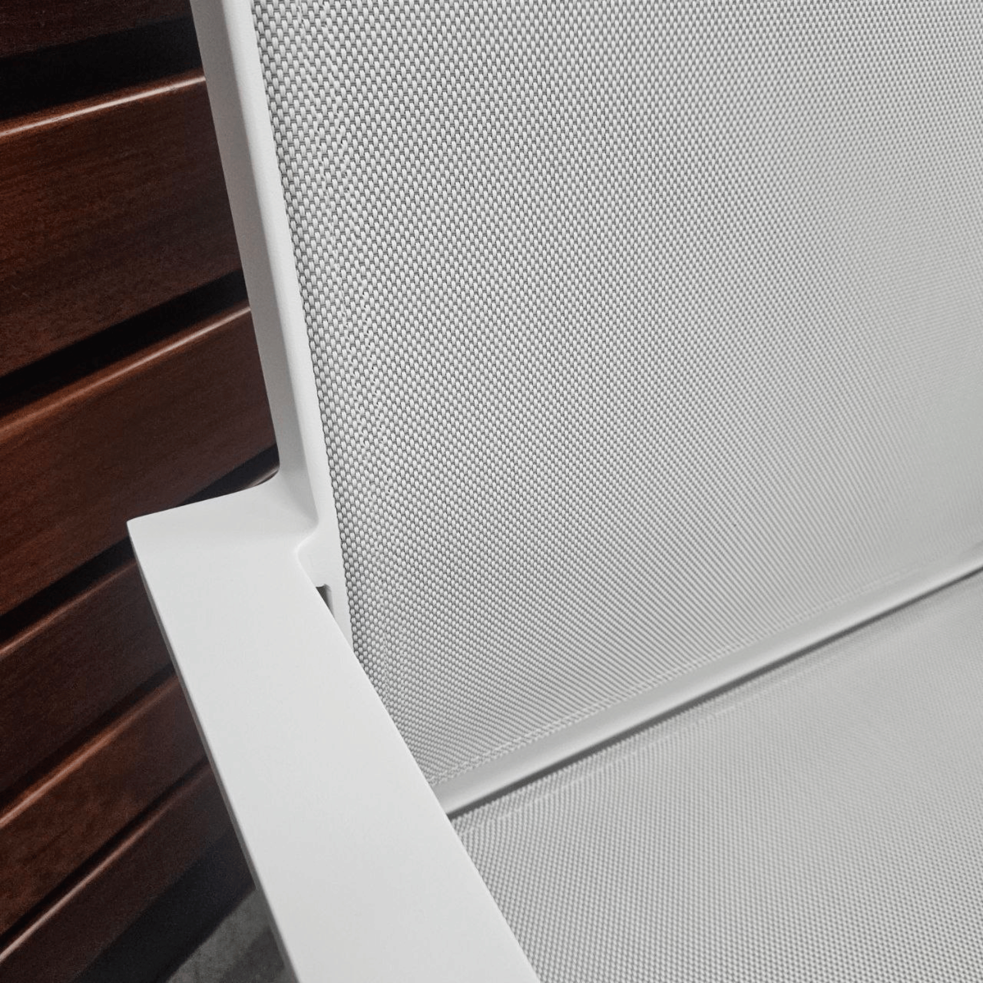 Close-up detail of a modern white chair with a textured mesh backrest and armrest, positioned next to a dark brown wooden slatted surface.