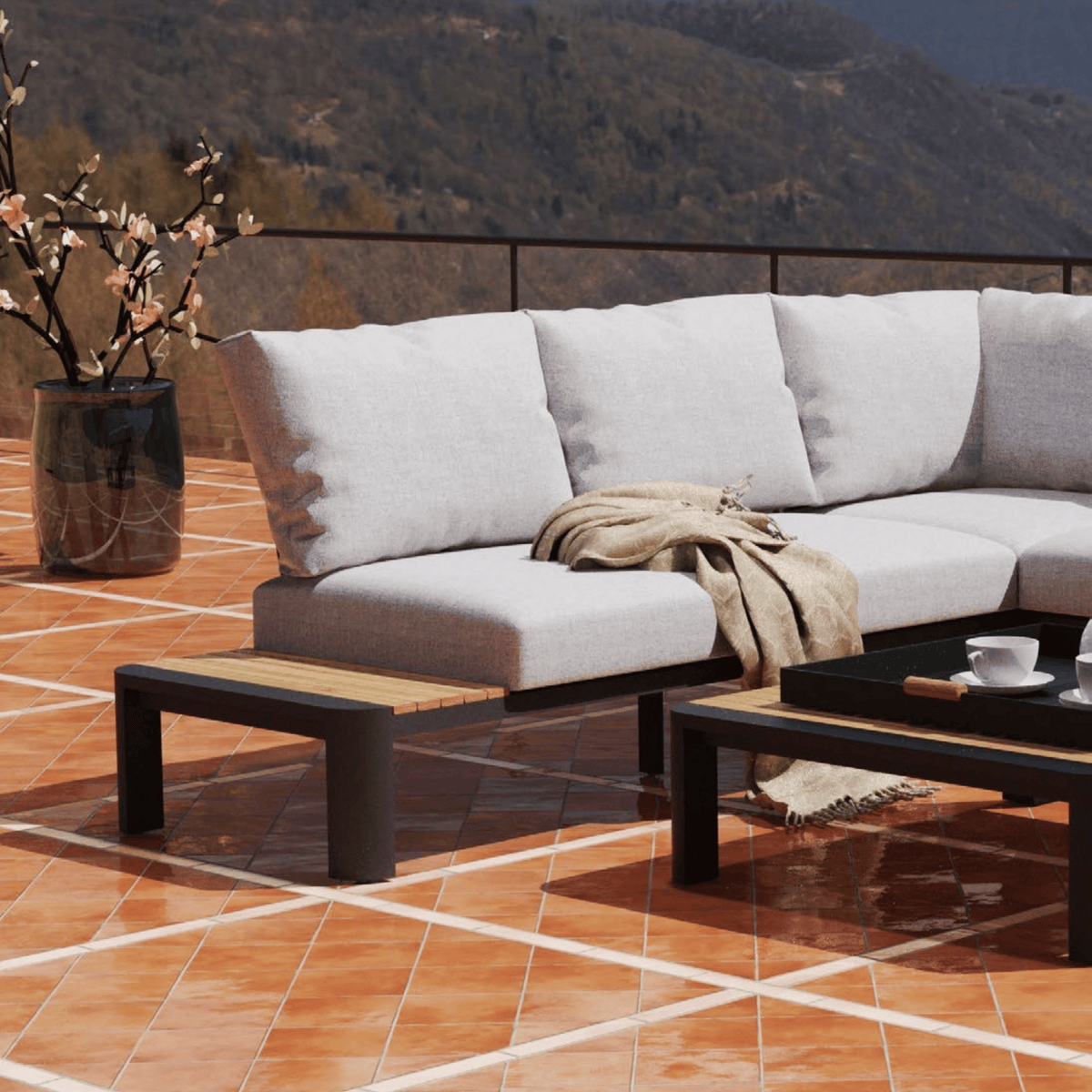 Outdoor sectional sofa with a beige throw blanket, set on a terracotta tiled terrace with a coffee table and mountains in the background.