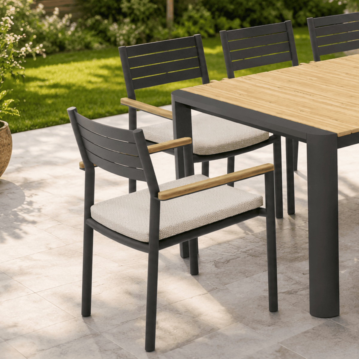 Outdoor dining set featuring a rectangular table with a light wood top and dark grey frame, surrounded by matching slatted chairs with light beige seat cushions on a stone patio.
