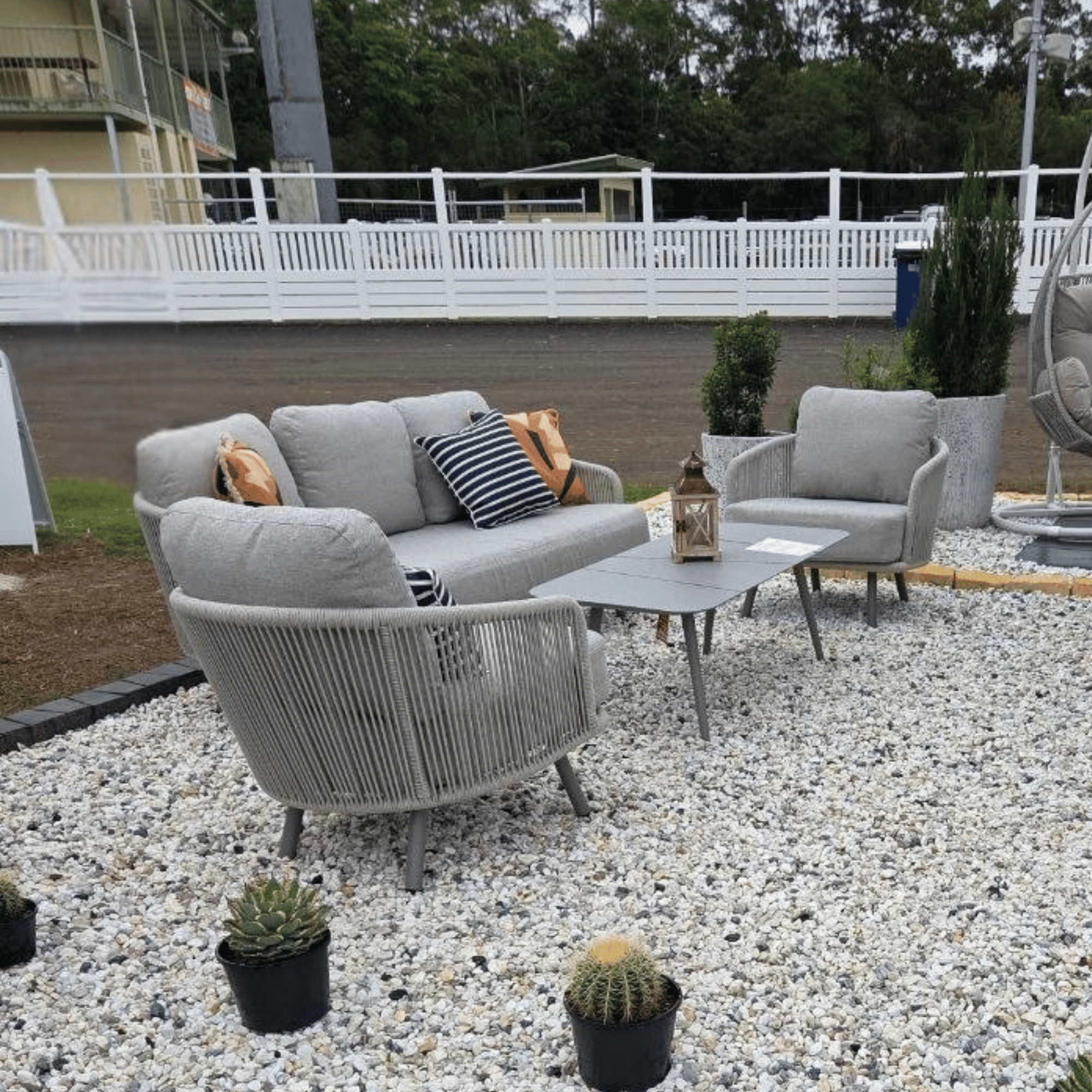 Outdoor Valencia 4pce Lounge Setting  including 2 grey rope armchairs, a matching grey sofa, and a grey coffee table on a gravel patio.