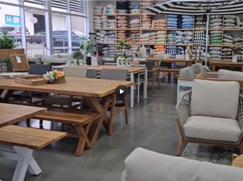 Furniture store with wooden tables, chairs, and cushions on display.